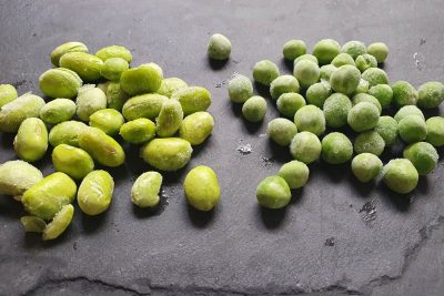 Tiefgekühlte Edamame und Erbsen liegen auf einem schwarzen Untergrund.