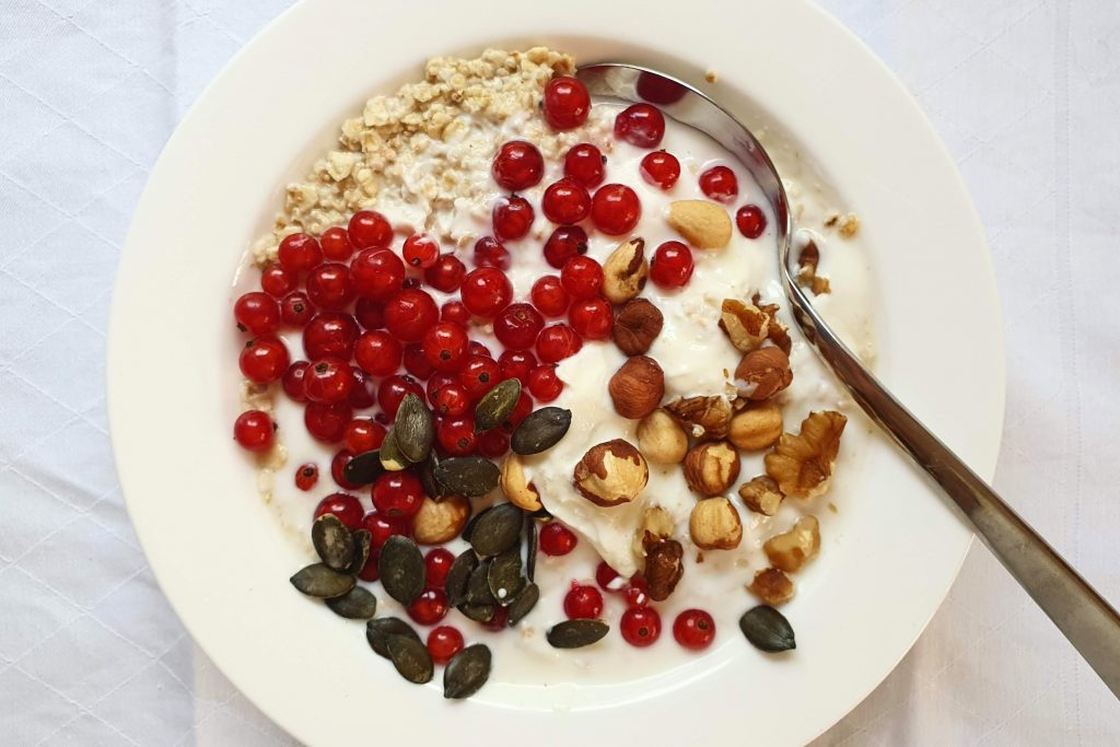 Eine Portion Quark mit Haferflocken, Johannisbeeren, Nüssen und Kürbiskernen in einem weißen Teller.