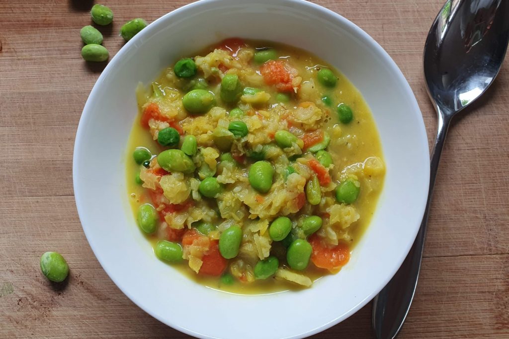 Eine weiße Schüssel mit Eintopf und grünen Edamame.